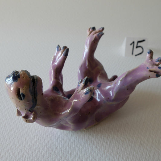 Handcrafted ceramic animal figurine "The Playful Creature (#15)" in stoneware by Nikolaj Jesper Cyon. Depicts a whimsical creature rolling on its back with paws in the air, finished in a glossy lavender-pink glaze with dark blue spots.