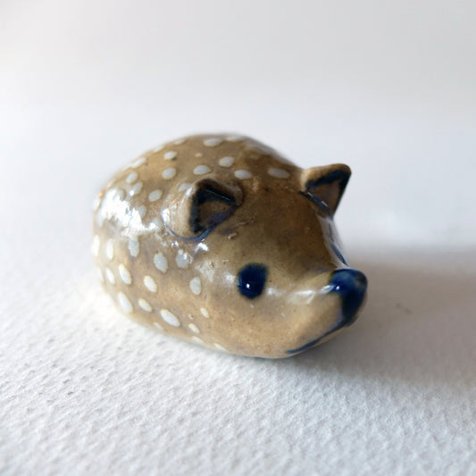 Handcrafted ceramic hedgehog figurine "The Polka Dotted Hedgehog (#25)" in stoneware by Nikolaj Jesper Cyon. Small rounded hedgehog sculpture in a warm tan glaze with delicate white polka dots and cobalt blue facial features.
