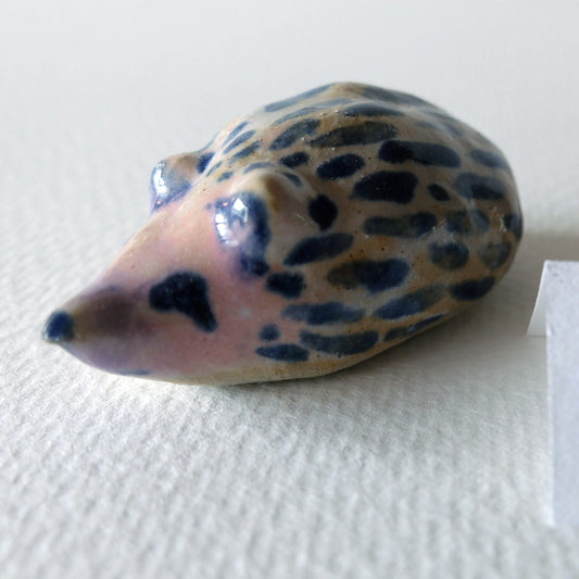 Handcrafted ceramic hedgehog figurine "The Striped Hedgehog (#3)" in stoneware by Nikolaj Jesper Cyon. Glazed with dark blue spots and stripes over a light pinkish beige body, with a glossy glaze finish.