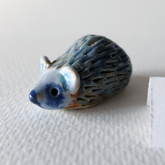 Handcrafted ceramic hedgehog figurine "The Timid Jade-Gazer (#1)" in stoneware by Nikolaj Jesper Cyon. Glazed with a shiny blue, white, and turquoise glaze on a terracotta stoneware body, with a textured pattern of indentations suggesting quills.