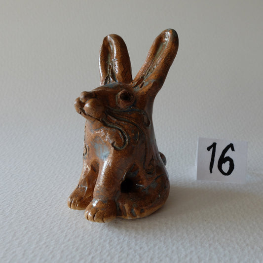 Handcrafted ceramic hare figurine "The Vain Hare (#16)" in stoneware by Nikolaj Jesper Cyon. Seated posture with long upright ears, a funny haughty expression with nose tilted up, and a warm earthy brown glaze with subtle blue highlights.