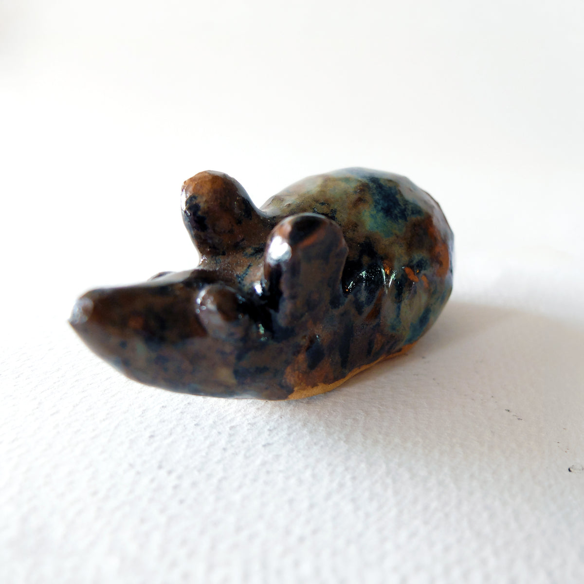 Handcrafted ceramic mouse figurine "The Zen Mouse (#23)" in stoneware by Nikolaj Jesper Cyon. Minimalist mouse sculpture inspired by classical Japanese art, finished in glossy variegated earthy brown, ochre, and deep blue-green glazes.